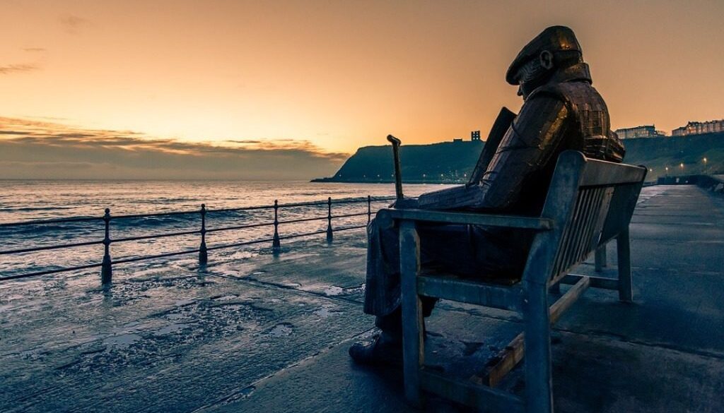 scultura di vecchio su panchina davanti al mare