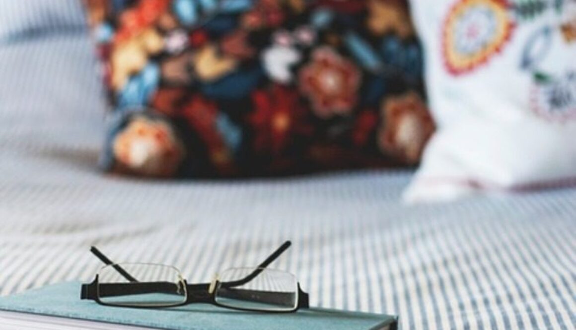 libro e occhiali sul letto con sfondo di cuscini