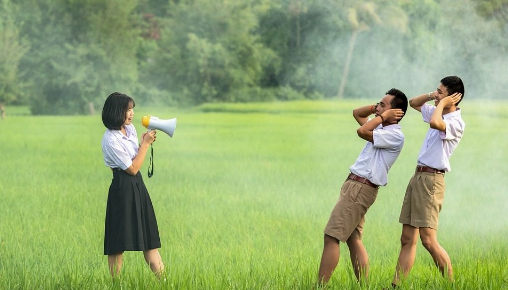 ragazza che parla con megafono e due ascoltatori che si tappano le orecchie