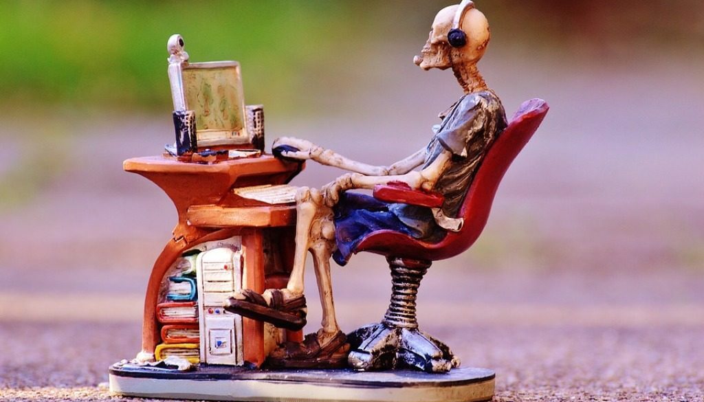 pupazzetto scheletro seduto davanti a un pc