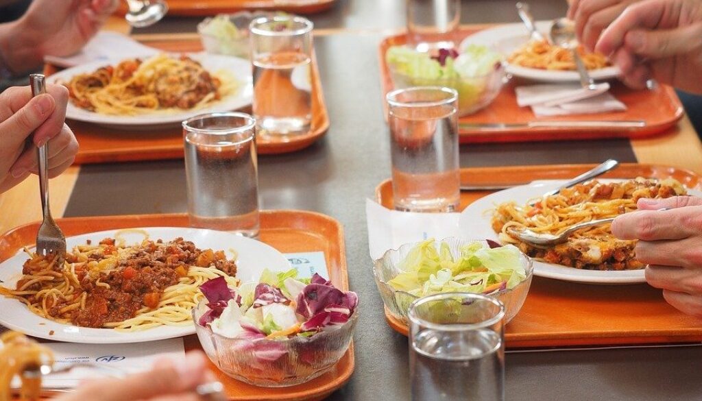 primo piano di tavolo di mensa con piatti e commensali