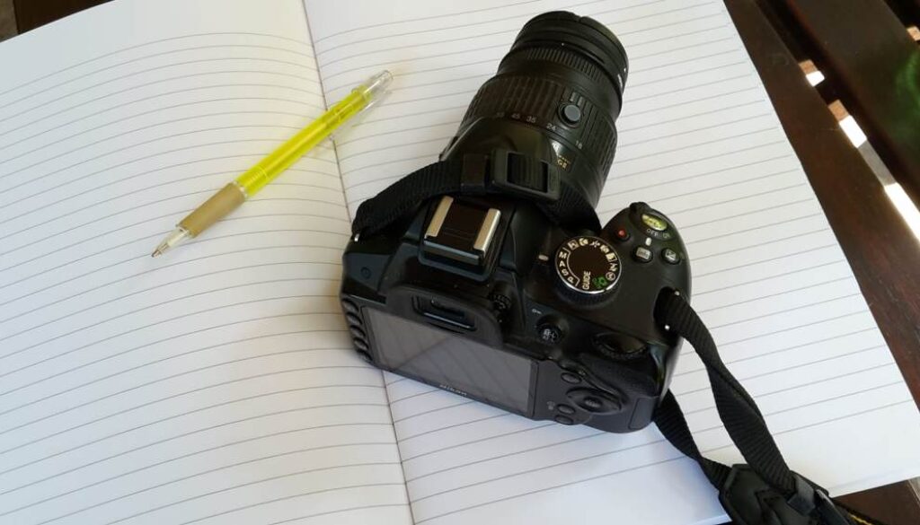 macchina fotografica, quaderno a righe, penna