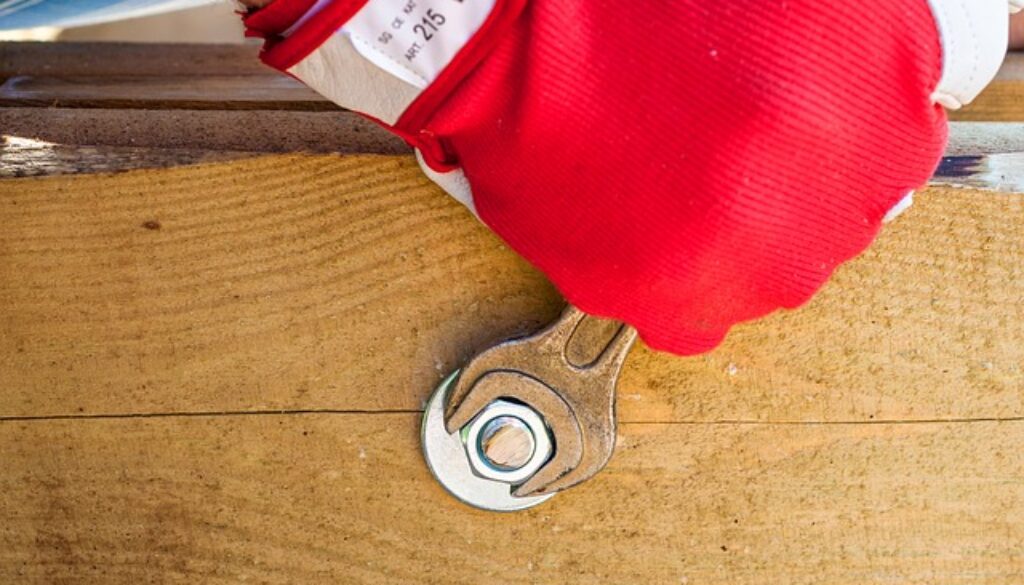 mano con guanto da lavoro rosso e chiave inglese