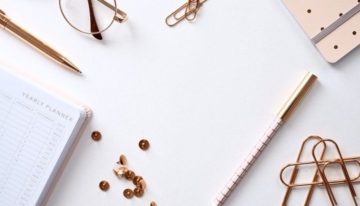 scrivania bianca con matita, occhiali, graffette e puntine dorati