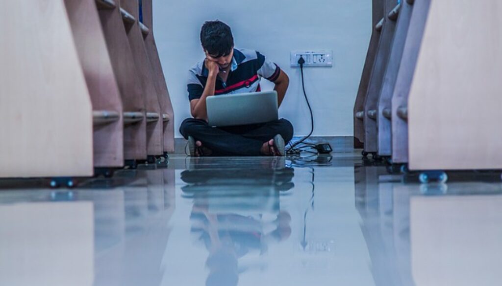 ragazzo che studi seduto per terra con portatile sulle gambe. quando la ricerca del lavoro non dà risultati si possono svolgere tante attività